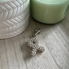 Silver beaded charity ribbon shaped keyring on a wooden surface with a potted plant and candle in the background.